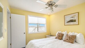 Une chambre à coucher avec un lit, un ventilateur de plafond, une fenêtre donnant sur un beau paysage et un tableau encadré accroché au mur.