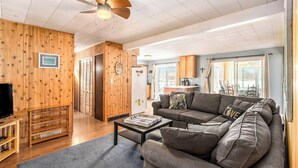 Un salon chaleureux avec un mur en bois, un ventilateur de plafond, un canapé et un téléviseur.