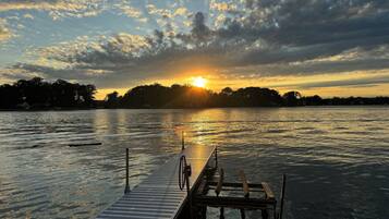 A wooden dock extending into calm water with a sunset in the background.