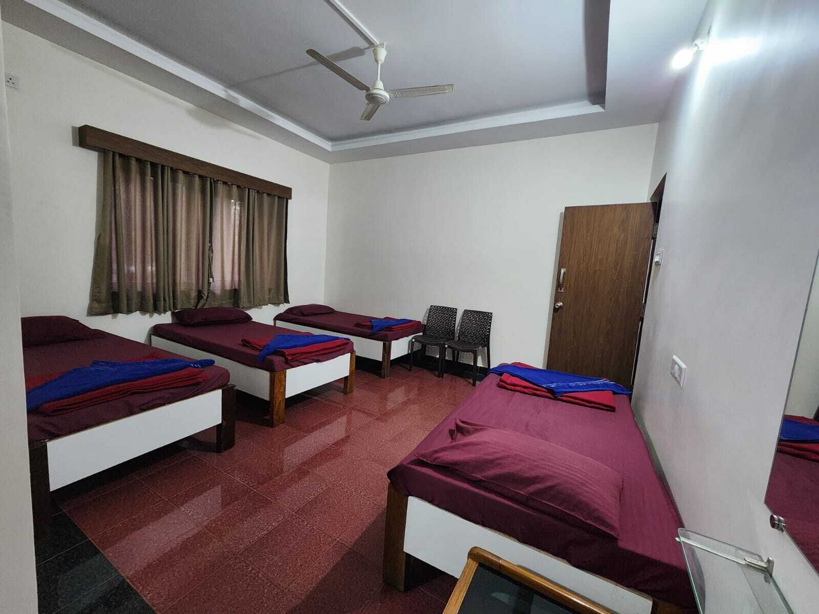A dormitory room with four single beds, a ceiling fan, a window with curtains, and a door.