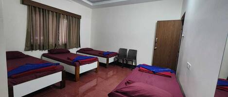 A dormitory room with four single beds, a ceiling fan, a window with curtains, and a door.