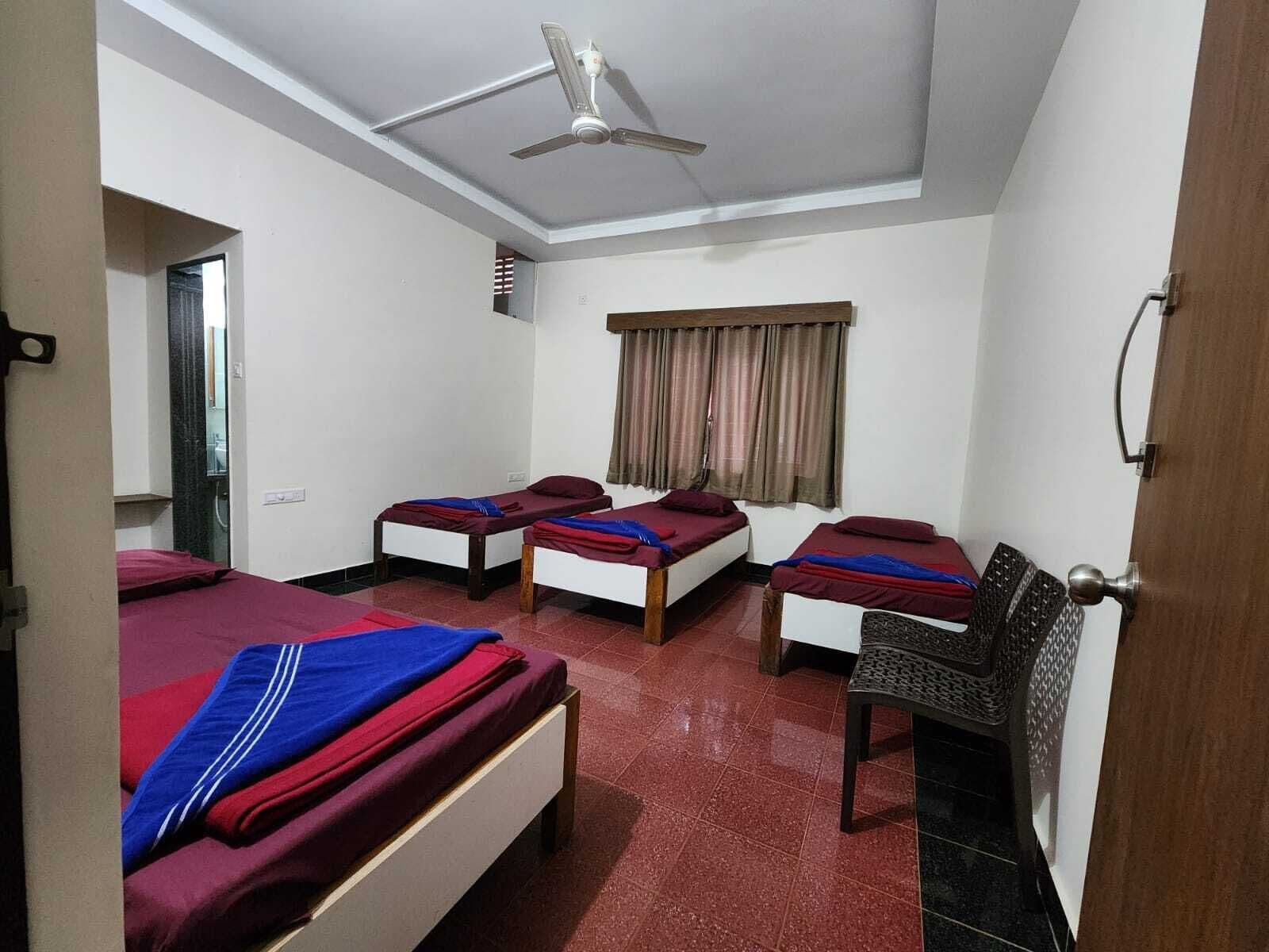 A hotel room with three single beds, a ceiling fan, a window with curtains, and a door.