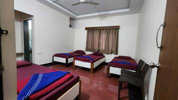 A hotel room with three single beds, a ceiling fan, a window with curtains, and a door.