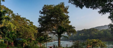 Un área de estar al aire libre con mesas, sillas, un hogar para fuego y vistas a un lago y colinas.