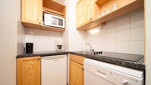 A compact kitchen with wooden cabinets, a microwave, a coffee maker, a dishwasher, and a sink. - Apartment in Alps near Ski Slopes (Allos)