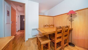 A dining area with a wooden table and chairs, a red lamp, and a wooden wardrobe. - Apartment in Alps near Ski Slopes (Allos)