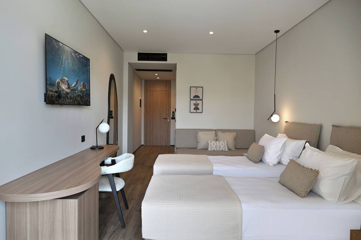Ein modernes Hotelzimmer mit Schreibtisch, zwei Betten, einem Sessel und Bildern an der Wand.