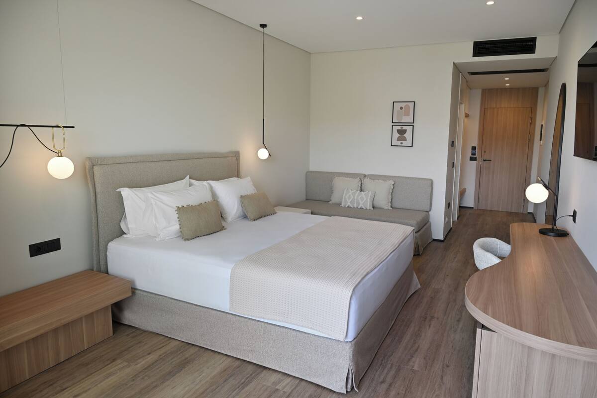 Ein modernes Hotelzimmer mit einem großen Bett, Nachttischen, einem Schreibtisch und einem Spiegel.