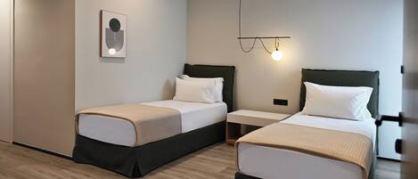 A modern hotel room with two beds, a bedside table, a wall-mounted light, and a framed picture.