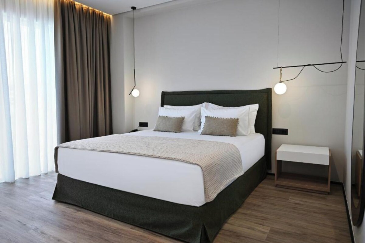 A modern hotel room with a large bed, bedside tables, and a view of the outdoors.