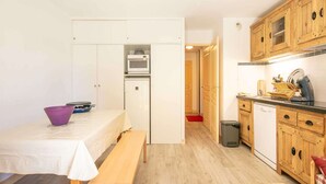 A compact kitchen with wooden cabinets, a microwave, and a dishwasher. There is a dining table with a bench and a purple bowl. - Apartment in Saint-Sorlin near Ski Resort (Saint-Sorlin-d´Arves)
