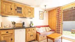 A compact kitchen with wooden cabinets, a dishwasher, and a dining area with a wooden table and bench. - Apartment in Saint-Sorlin near Ski Resort (Saint-Sorlin-d´Arves)