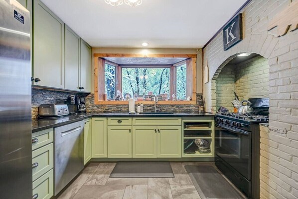 A compact kitchen with green cabinets, a built-in stove, and a window overlooking a forest.