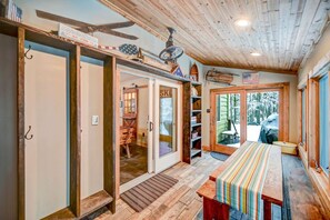 A rustic cabin interior with a wooden ceiling, a dining table with a striped tablecloth, and a view of a snowy landscape through the door.