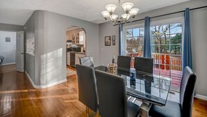 Un espace de salle à manger moderne avec une table et des chaises en verre, un lustre et une vue sur une terrasse et un espace extérieur.