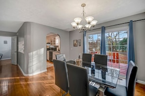 Ein moderner Essbereich mit einem Glastisch und Stühlen, einer Chandelüster und Blick auf eine Terrasse und Außenbereich.