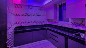 A modern kitchen with a checkered backsplash, a black countertop, and purple lighting. - Eastern Heights (Ranchi)