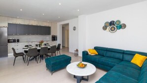 A modern living room with a teal sofa, a white coffee table, and a dining area with a kitchen in the background. - Luxury Villa Navis (Ploce)