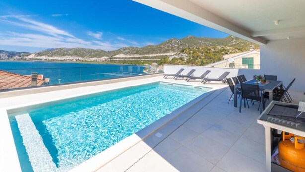 A rooftop pool with clear blue water, surrounded by lounge chairs and a dining area with a table and chairs. - Luxury Villa Navis (Ploce)