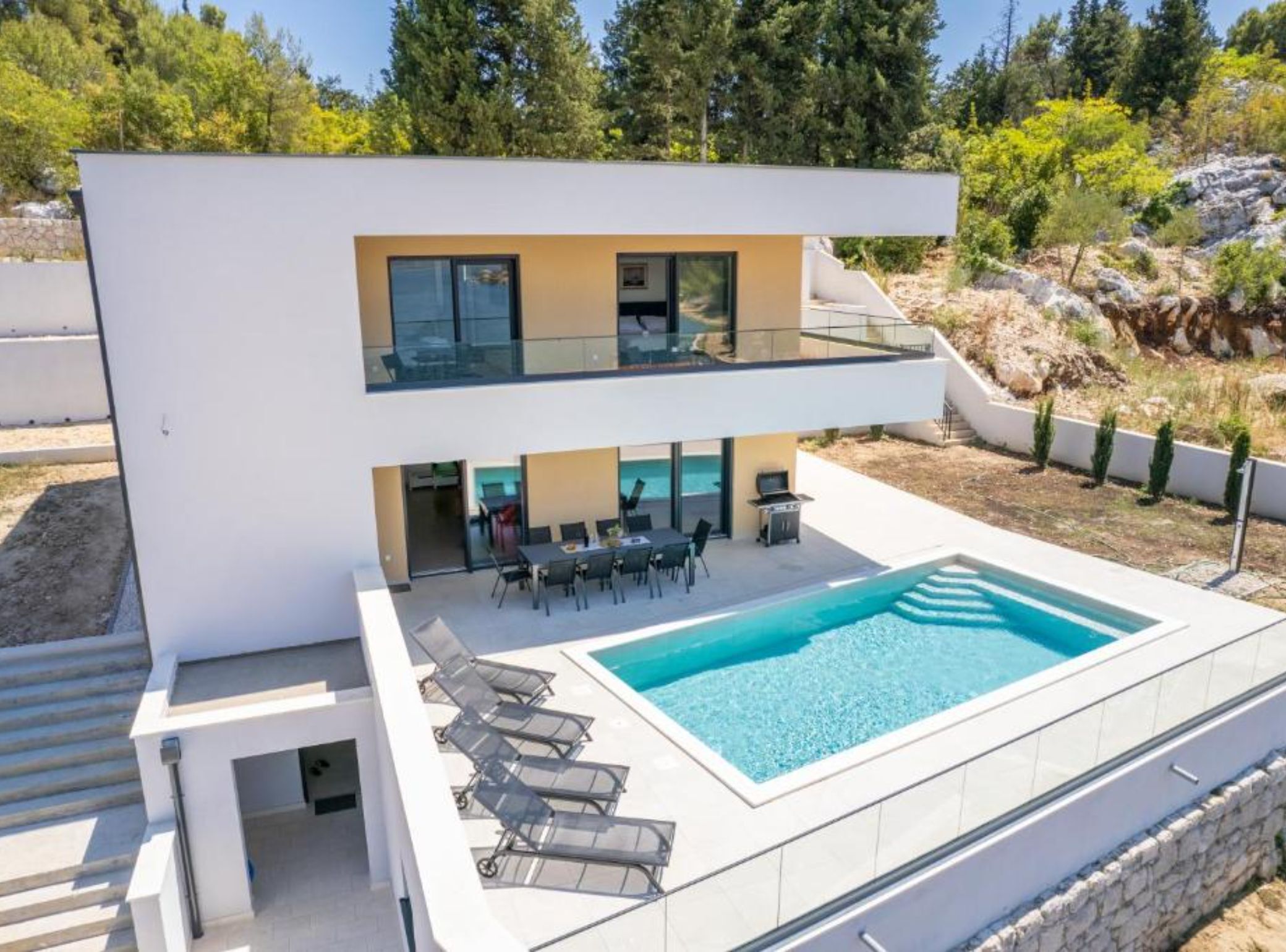 Uma casa moderna de dois andares com piscina, área de estar externa e vista para a paisagem ao redor.