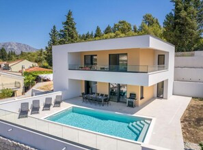 A modern two-story house with a swimming pool, outdoor seating, and a mountain backdrop. - Luxury Villa Navis (Ploce)