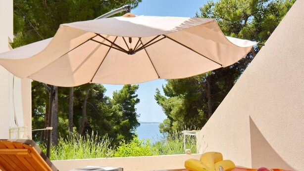Une table en bois avec un saladier de fruits et un parasol beige.