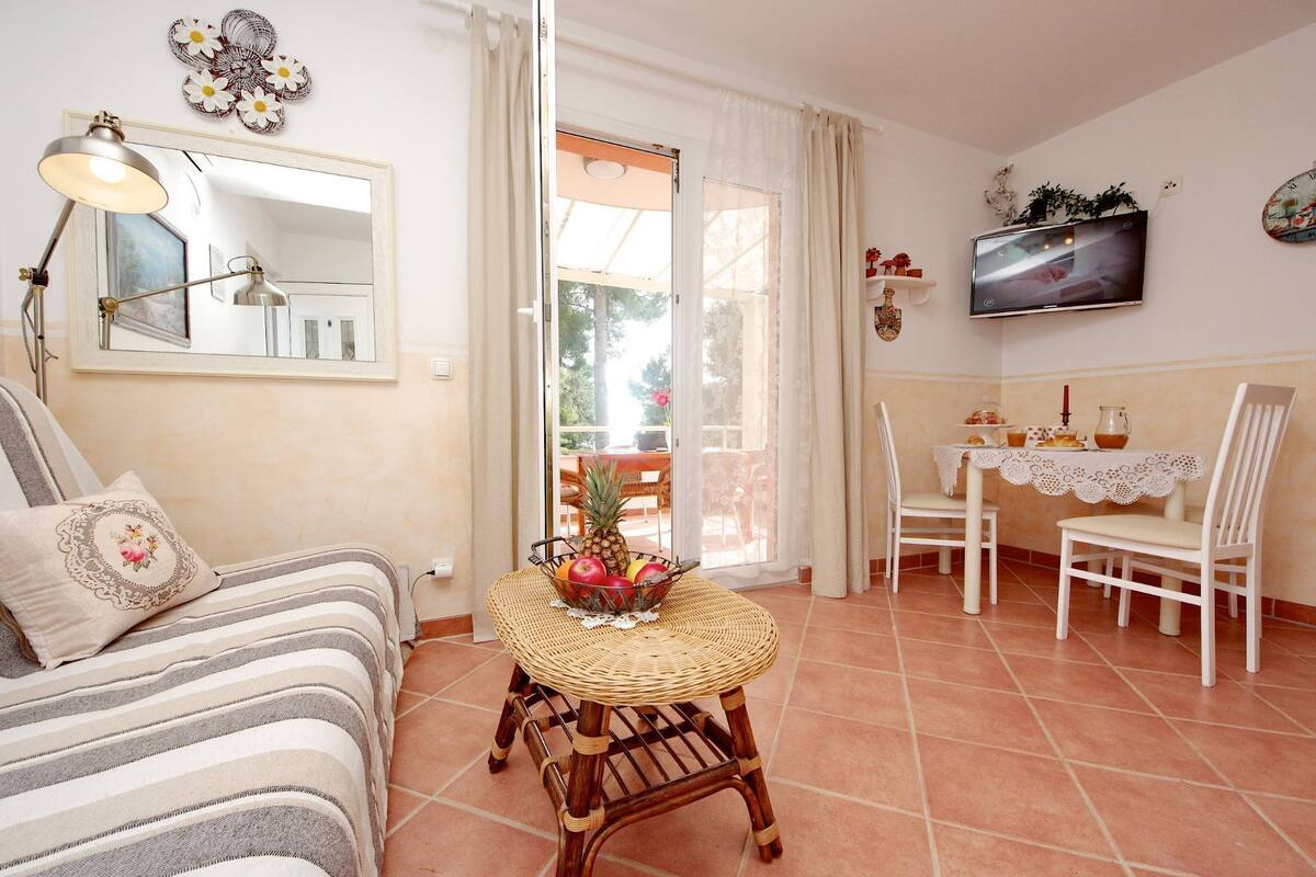 A cozy living room with a sofa, a wicker table with fruit, a TV, and a dining area with chairs and a table.