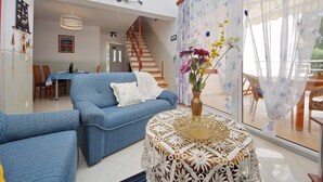 Un salon avec un canapé bleu, une table blanche ornée d’un vase de fleurs et un escalier menant à une autre pièce.