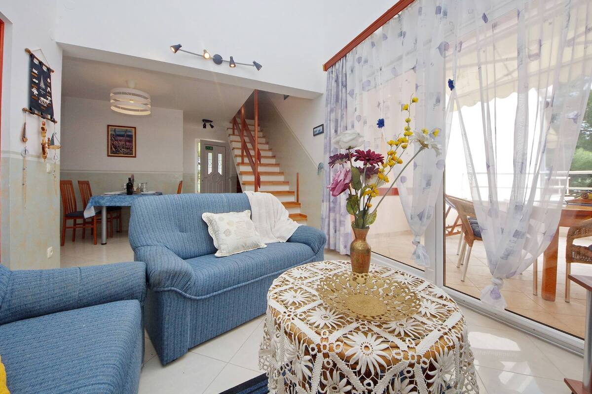 A living room with a blue sofa, a white table with a vase of flowers, and a staircase leading to another room.