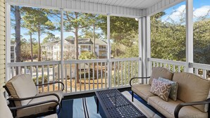 A covered porch with two chairs and a table, overlooking a residential area with trees and houses.