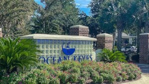 A sign with the name "Ocean Keyes" surrounded by lush greenery and a brick structure.