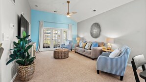 A living room with a blue accent wall, a ceiling fan, a sofa, a patterned armchair, and a large potted plant.