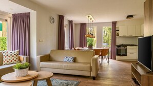 Una sala moderna con sofá, mesa de centro y comedor. Se observa una cocina con estufa y televisor.