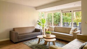 Una sala de estar con un sofá gris, una mesa de centro y un ventanal con vistas a la vegetación.