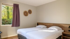 Un dormitorio con dos camas, una ventana con cortina morada y dos elementos decorativos en la pared.
