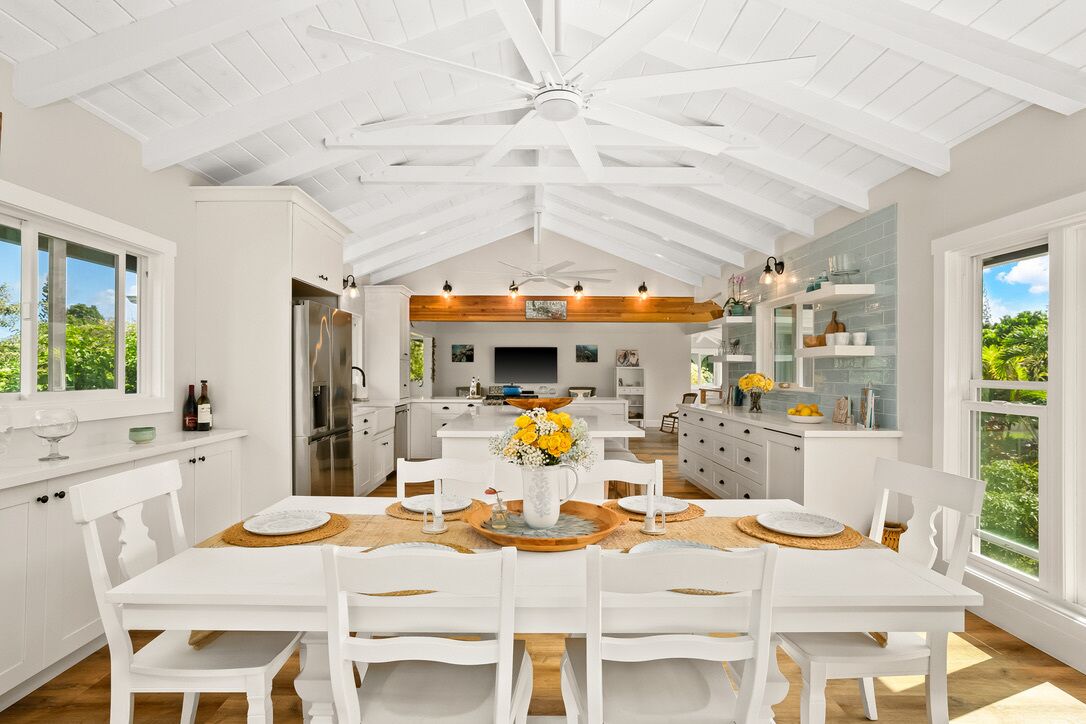 A spacious kitchen with white cabinetry, a central island, and a dining area with a white table and chairs.