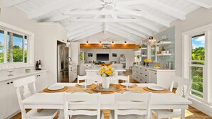 A spacious kitchen with white cabinetry, a central island, and a dining area with a white table and chairs. - Perfect Private Getaway Minutes to Hanalei Bay! (Princeville)