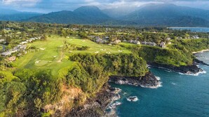 An aerial view of a coastal golf course with houses and a mountainous backdrop. - Perfect Private Getaway Minutes to Hanalei Bay! (Princeville)