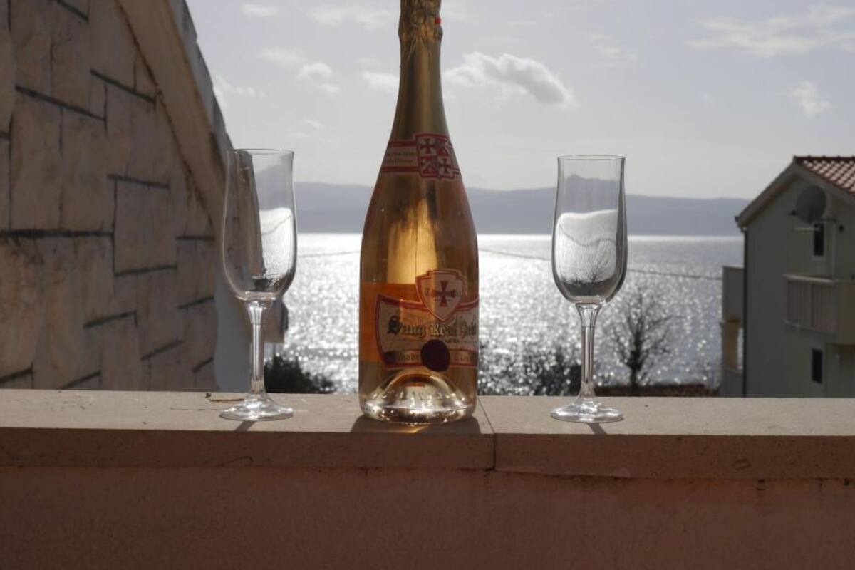Una botella de champán y dos copas sobre un alféizar, con vistas al agua y edificios al fondo.