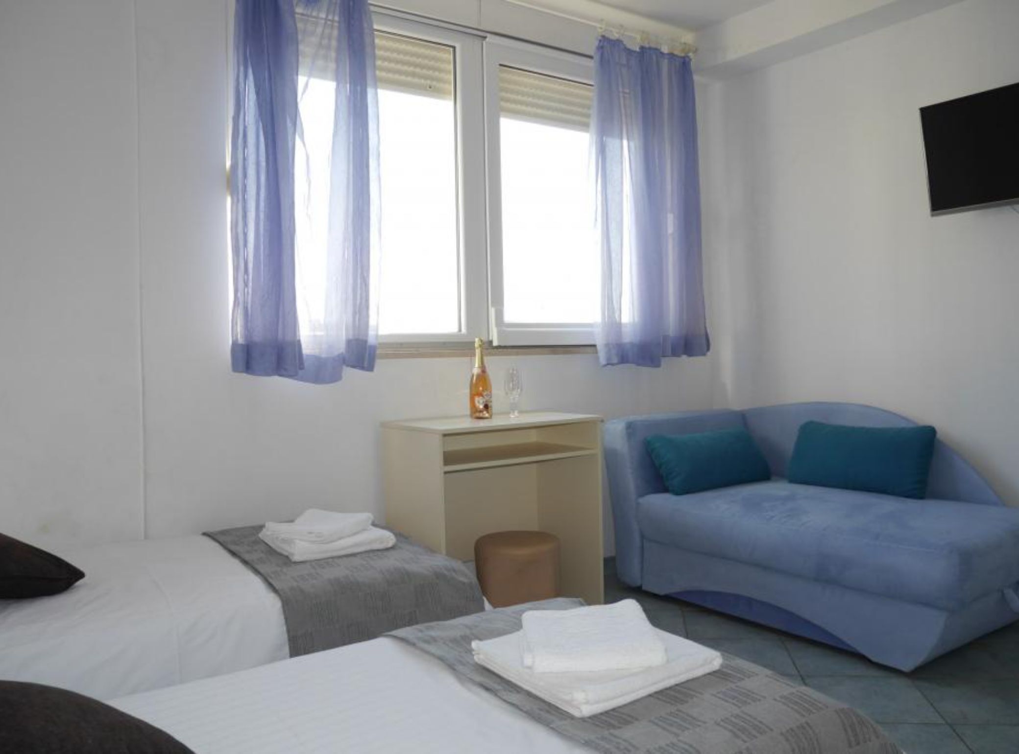 A hotel room with two beds, a desk, a blue sofa, and a TV on the wall.