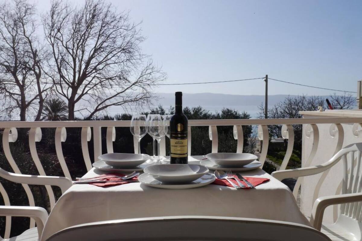 Mesa al aire libre con una botella de vino, platos y cubiertos.
