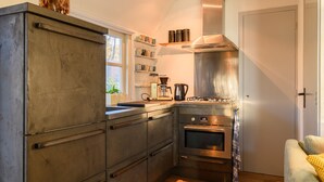 A compact kitchen with a stove, oven, and coffee maker, and a window with a view of trees. - Luxurious bungalow for 2 persons (Herpen)