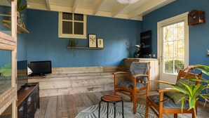 A cozy room with a blue wall, wooden bench seating, a television, and a large window. - Luxurious bungalow for 2 persons (Herpen)