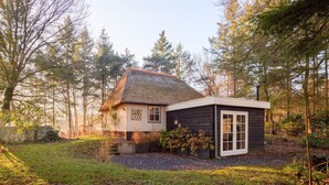 A rustic house with a thatched roof, surrounded by trees and a gravel driveway. - Luxurious bungalow for 2 persons (Herpen)