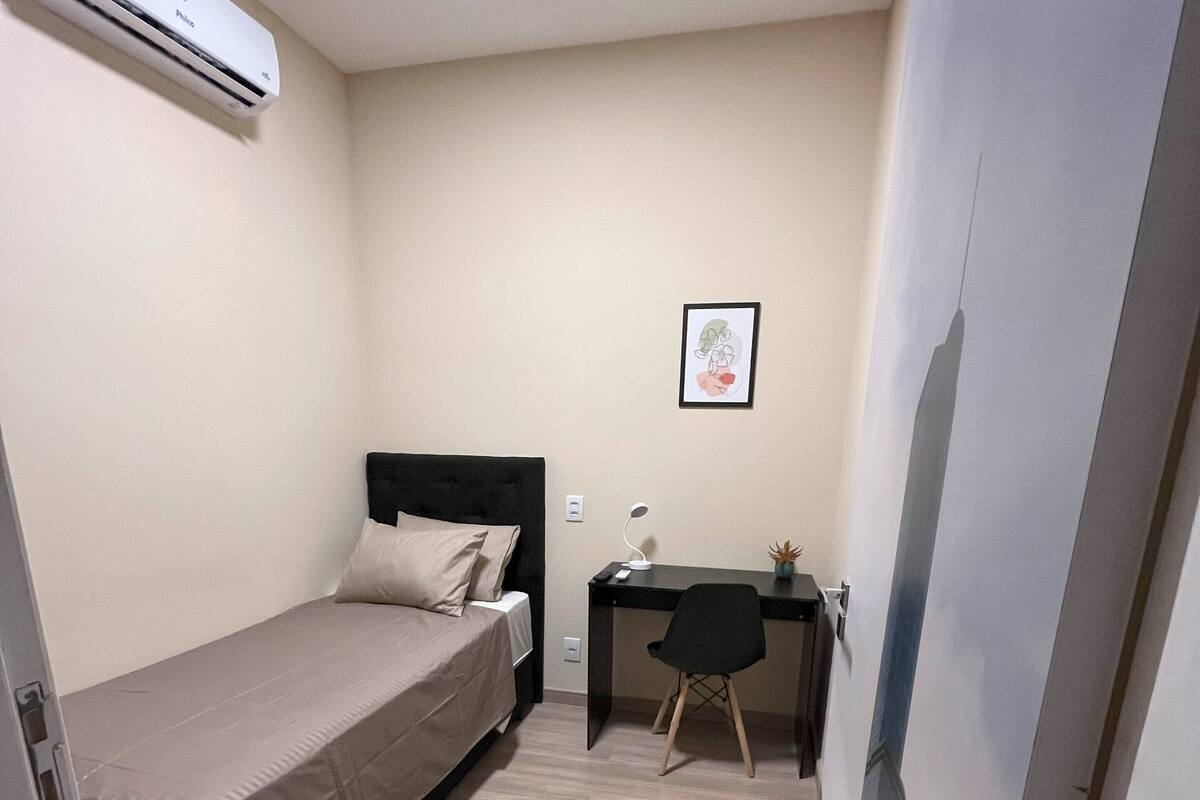 Une petite chambre à coucher, bien rangée, avec un lit, une table de chevet, un bureau et une chaise.
