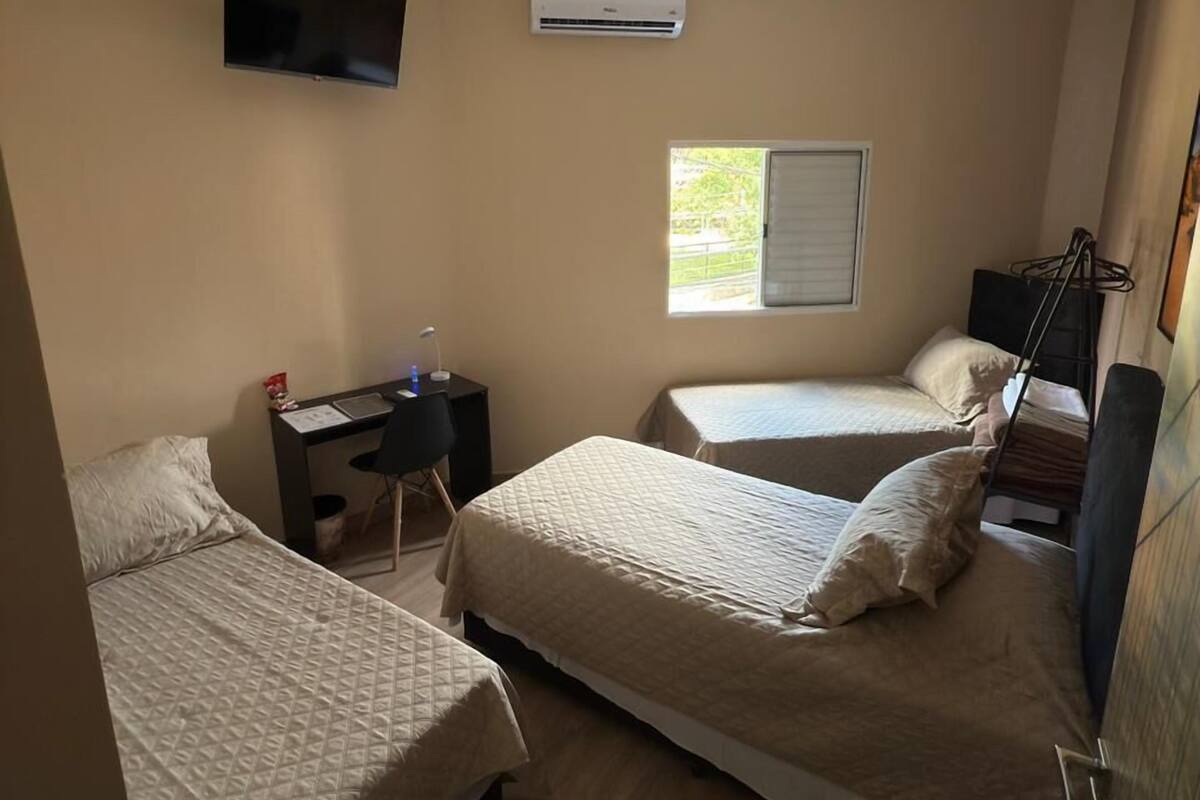 Une chambre avec deux lits, un bureau, une télévision, un climatiseur et une fenêtre.