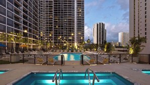 Uma área de piscina de hotel com várias piscinas, espreguiçadeiras e um edifício alto ao fundo.