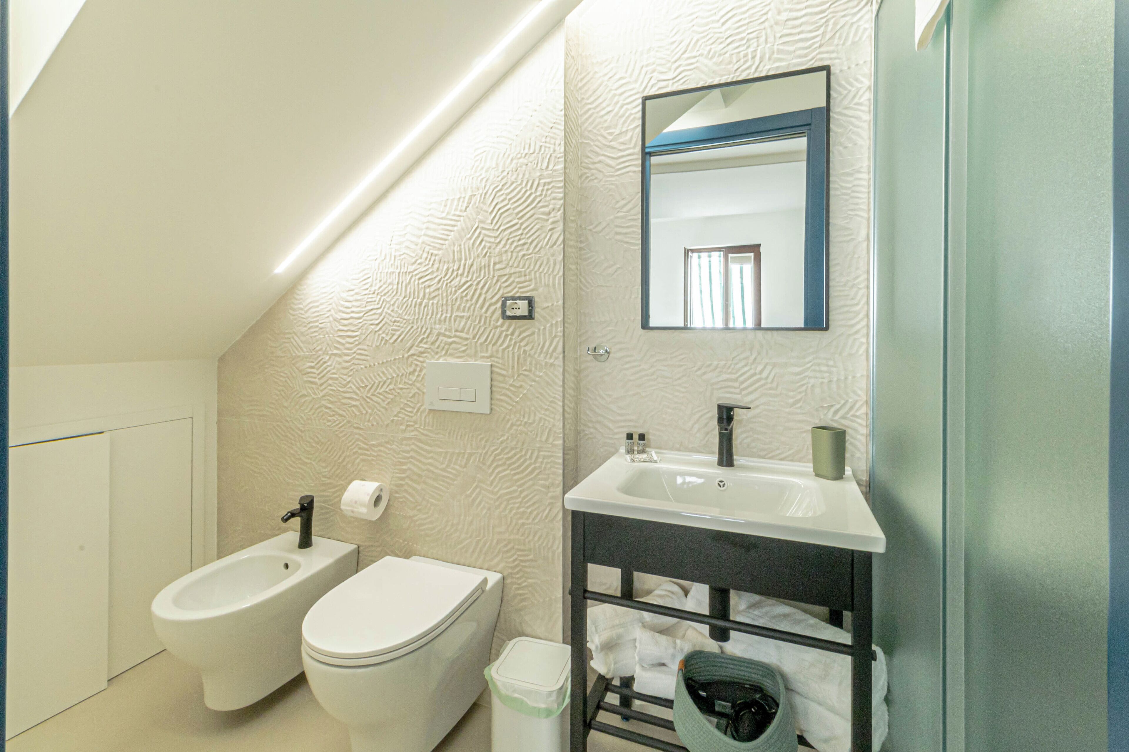 Un bagno moderno con bidet, toilette, lavandino e portasciugamani.