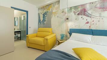 Un dormitorio moderno con cama, un sillón amarillo, un cuadro abstracto grande en la pared y un baño visible a través de una puerta abierta.