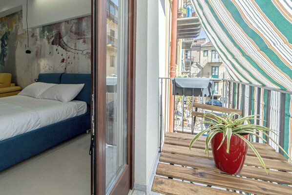 A bedroom with a bed, a window, and a balcony with a potted plant. - Jura Haus - A Light-Filled Apartment 5 Minutes from the Historic Center, New and Cozy (Castelbuono)